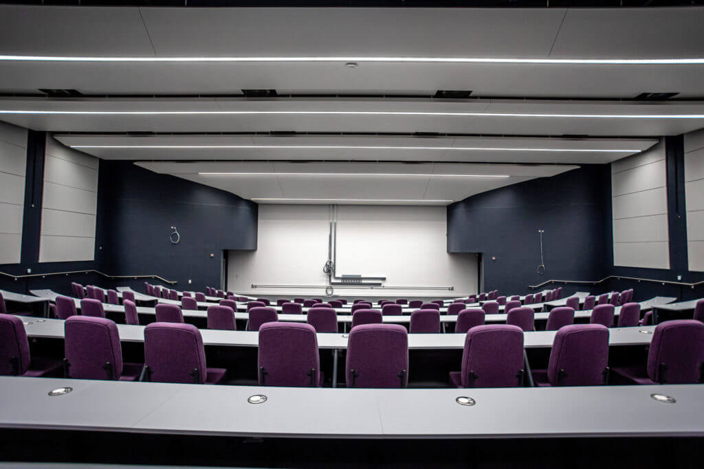 Picture of a seating lecture hall featuring multiple rows of purple-cushioned seating.
