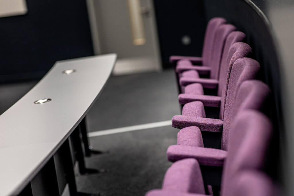 Picture of a lecture hall featuring multiple rows of purple-cushioned seating.