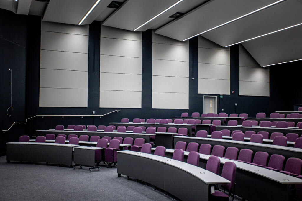Picture of a interactive seating lecture hall featuring multiple rows of purple-cushioned seating.